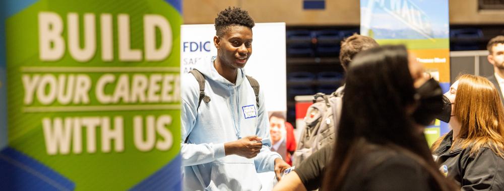 Student stands neat career fair banner.