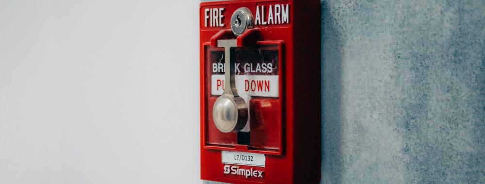 A red fire alarm is on a grey wall.